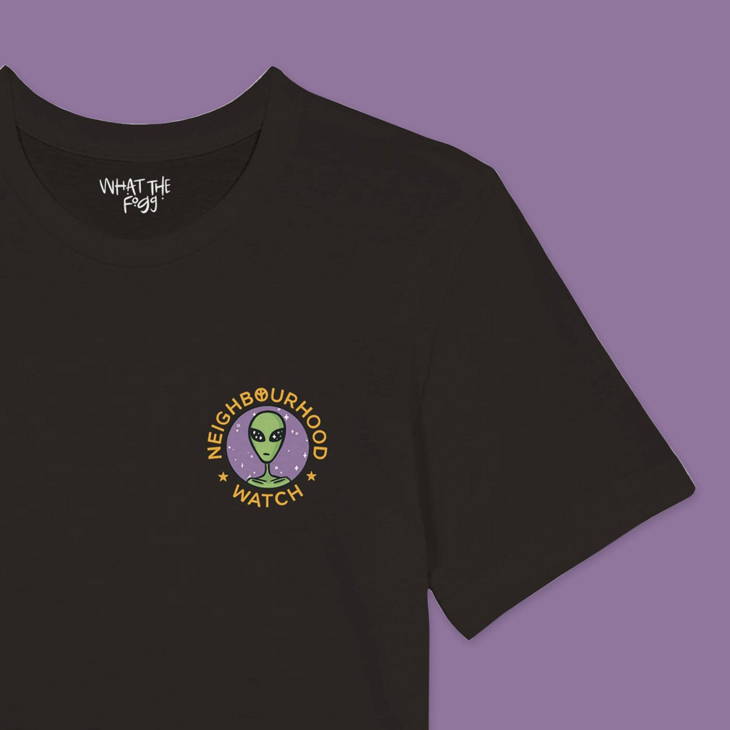 Close up of a Black t-shirt featuring a playful twist on the traditional Neighbourhood Watch poster. The front of the shirt displays a circular badge with a design of aliens instead of people. The badge is surrounded by the text 'Neighbourhood Watch' in a bold, eye-catching font.