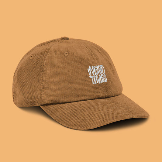 Front-side angle of a camel-coloured corduroy hat with 'Weird Times' printed in white on the front.
