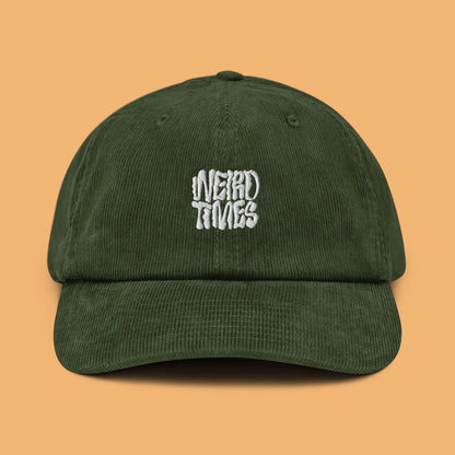 Front angle of a dark olive-coloured corduroy hat with 'Weird Times' printed in white on the front.